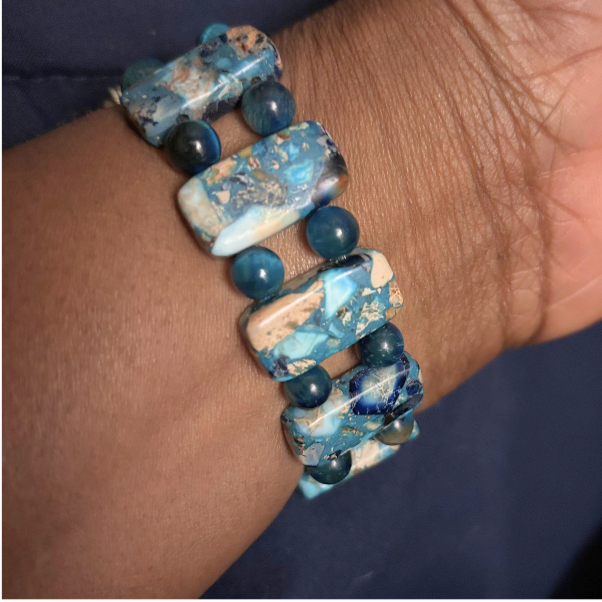 A close-up of a person's wrist wearing a beaded stretch bracelet made of blue and white marbled rectangular beads separated by dark blue round beads.